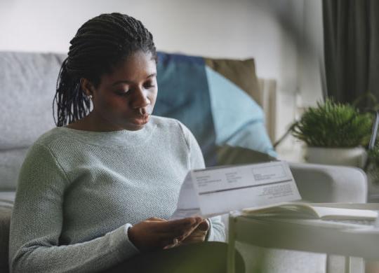 一个年轻的非裔美国女商人在家远程工作时阅读水电费账单的画像.